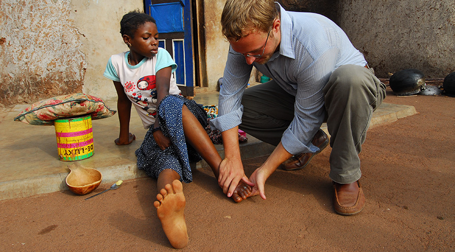 Adam Weiss, now director of the Carter Center’s Guinea Worm Eradication Program, treats a girl with an infected Guinea worm in her foot.