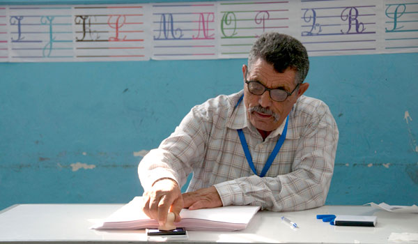 A poll worker stamps the back of an unmarked ballot before handing it to a voter.